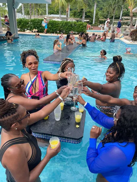 A group of women enjoy a celebratory toast at a swim-up bar in a tropical pool, highlighting the sense of community and connection.