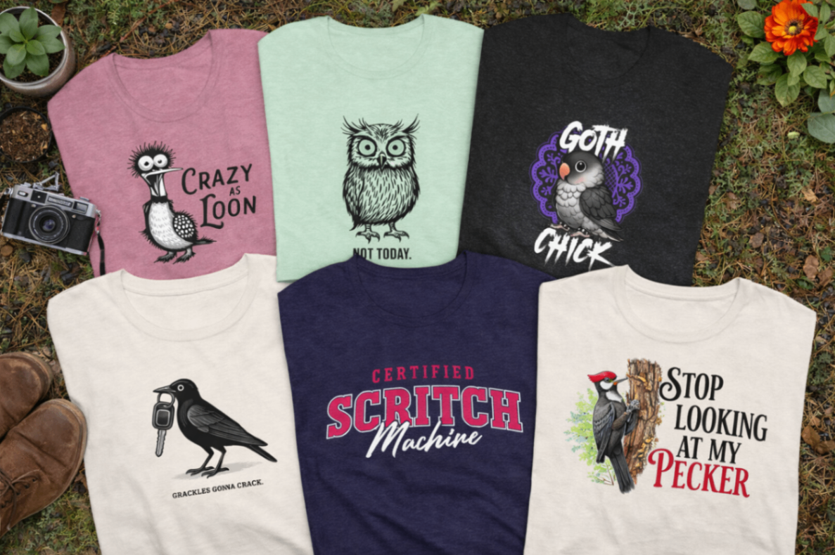 Birdwear T-Shirts Collection Six original Birdwear t-shirts featuring humorous, illustrated bird designs: a loon with 'Crazy as Loon,' an owl with 'Not Today,' a cockatiel with 'Goth Chick,' a grackle with 'Grackles Gonna Crack,' a bold text 'Certified Scritch Machine,' and a woodpecker with 'Stop Looking at My Pecker.' The shirts are arranged outdoors on grass, showcasing vibrant colors and playful bird-themed artwork.