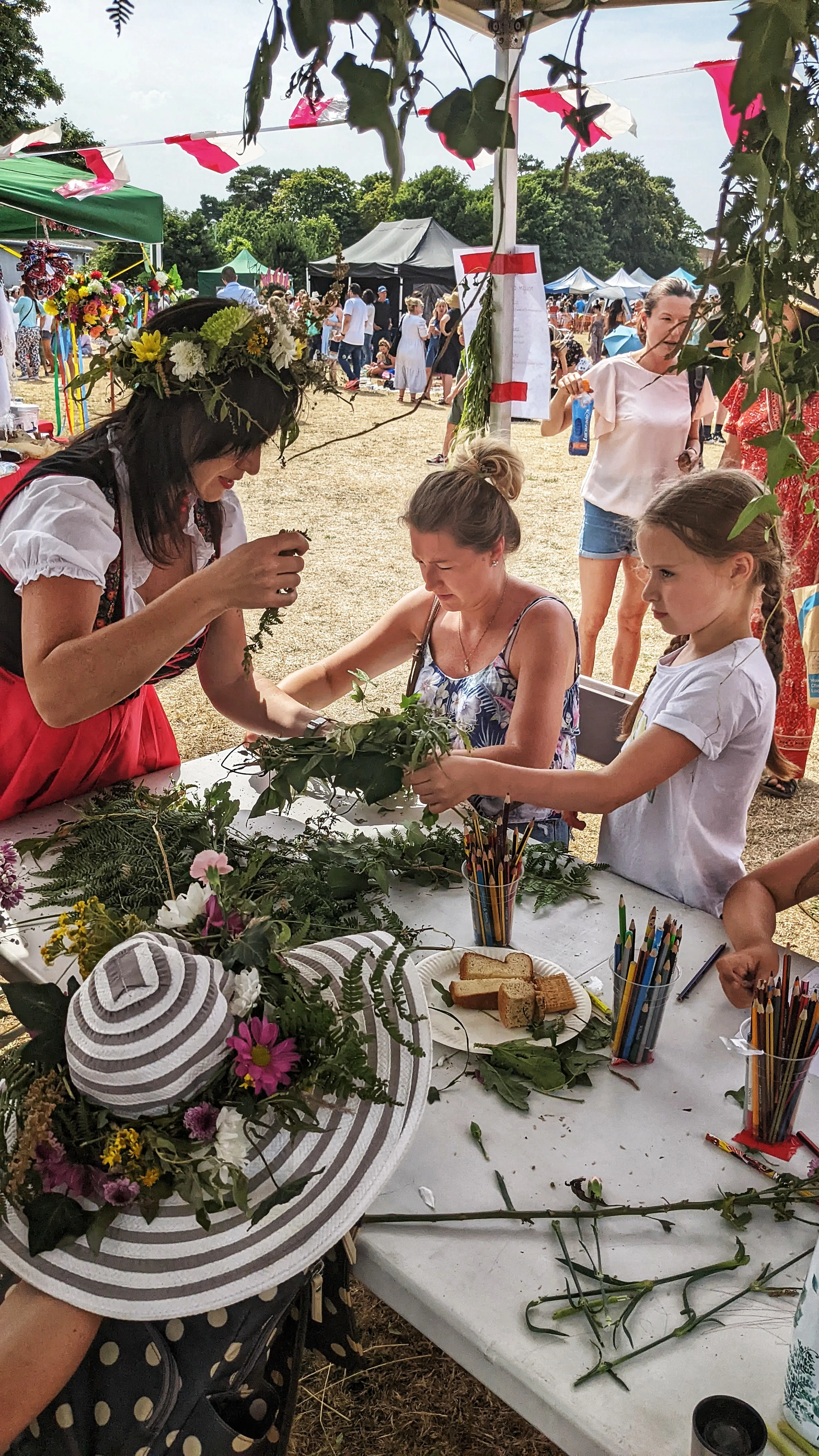 Families participate in a hands-on flower crown and nature craft workshop led by a woman in traditional dress.