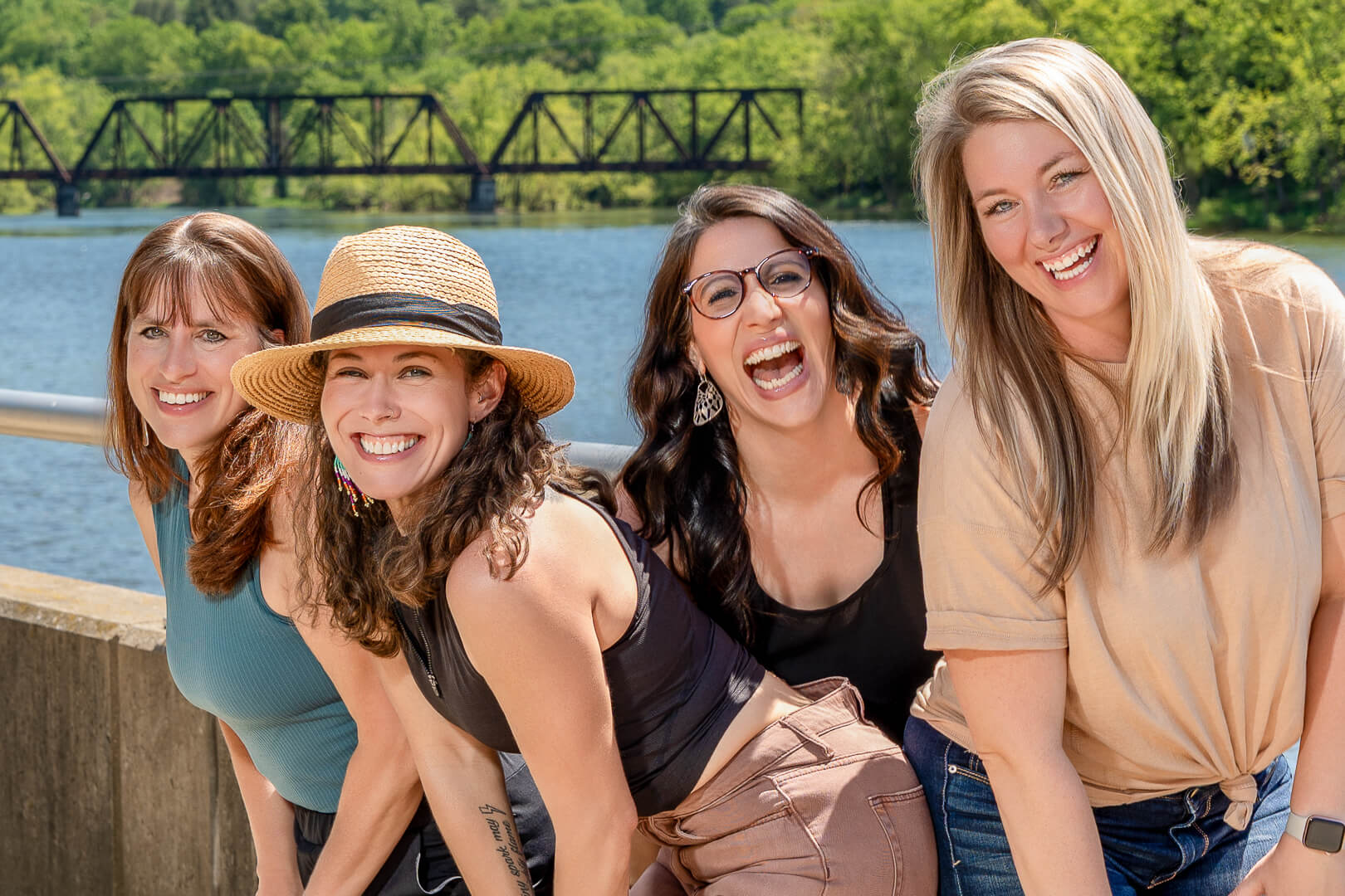 Four women laughing together outdoors by the river