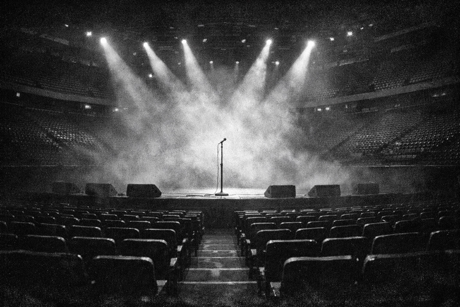 Dramatic black-and-white arena stage with spotlights on a lone microphone, honoring Elvis Presley’s live legacy.