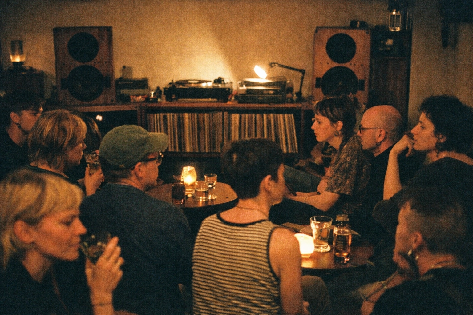 Inside a Neukölln listening bar: queer crowd in their 30s sitting quietly, amber light, turntable and big speakers, candid 35mm grain.