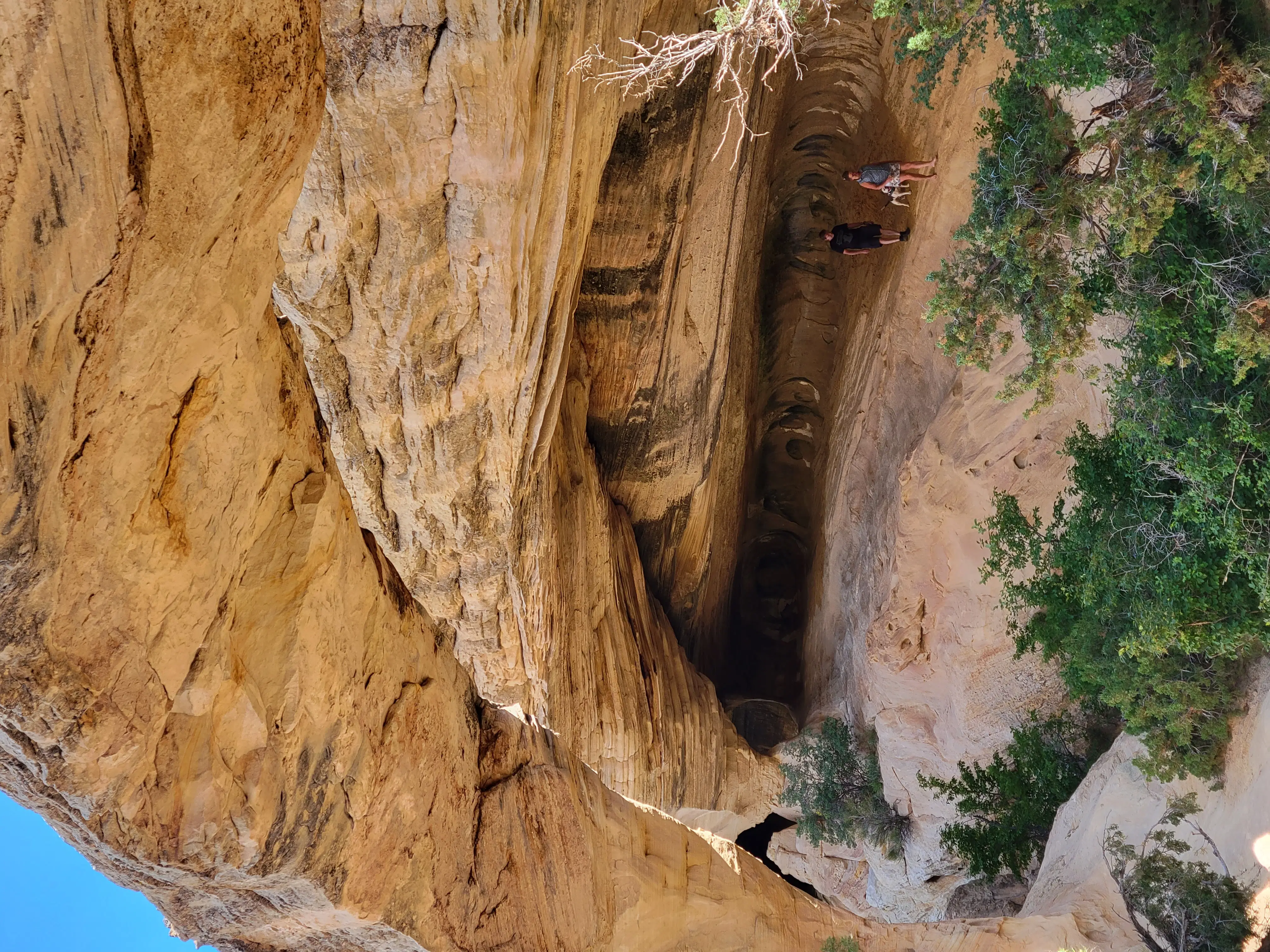 Two off-road adventurers stand beneath a massive sunlit sandstone arch in Utah