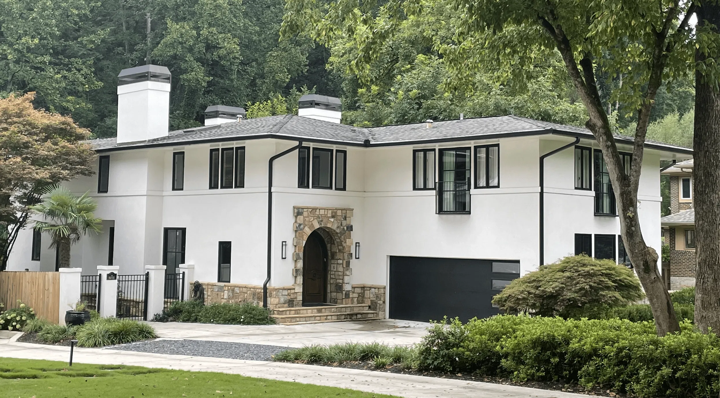 Modern two-story home with a fresh white exterior, crisp black trim and gutters, stone archway entrance, and contrasting black garage door and window frames.