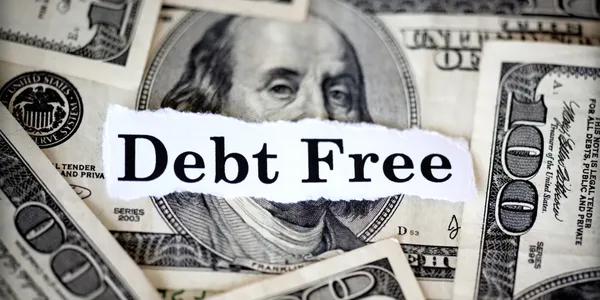 Debt Free A torn paper with the words 'Debt Free' is placed over multiple one hundred dollar bills, visually representing financial freedom, a key focus of our debt-free life strategies and personalized financial protection solutions.