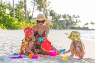 A mother and two young children playing on a white sandy Maldives beach.