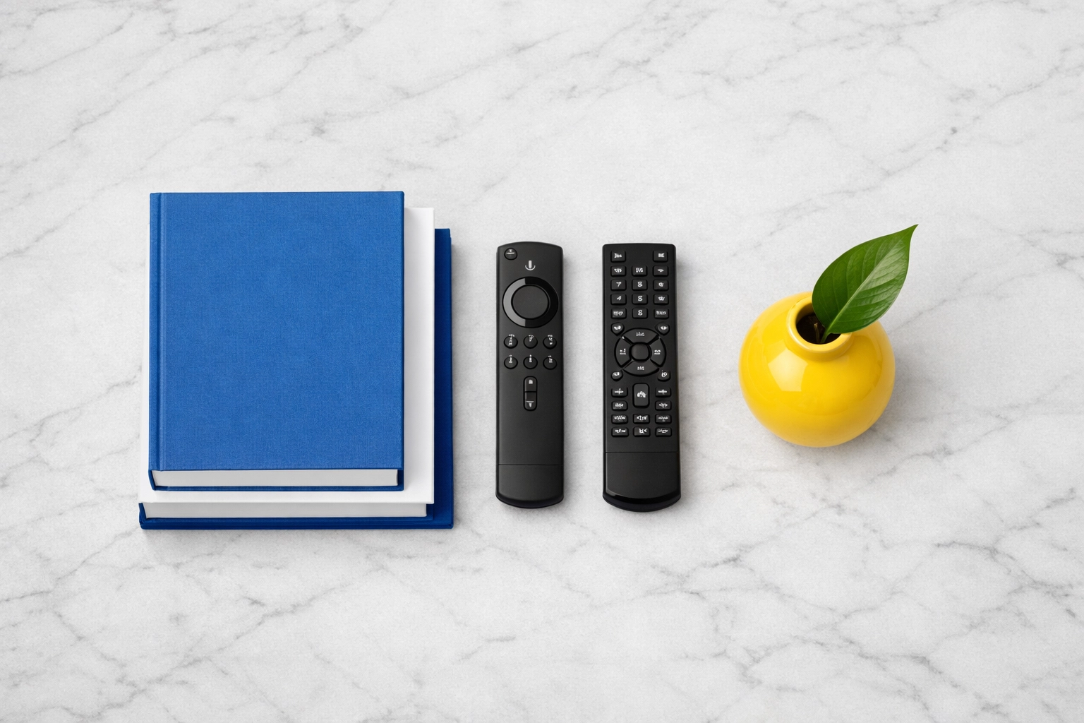 Neatly stacked books and organized remotes on a marble coffee table showing a tidy living space.