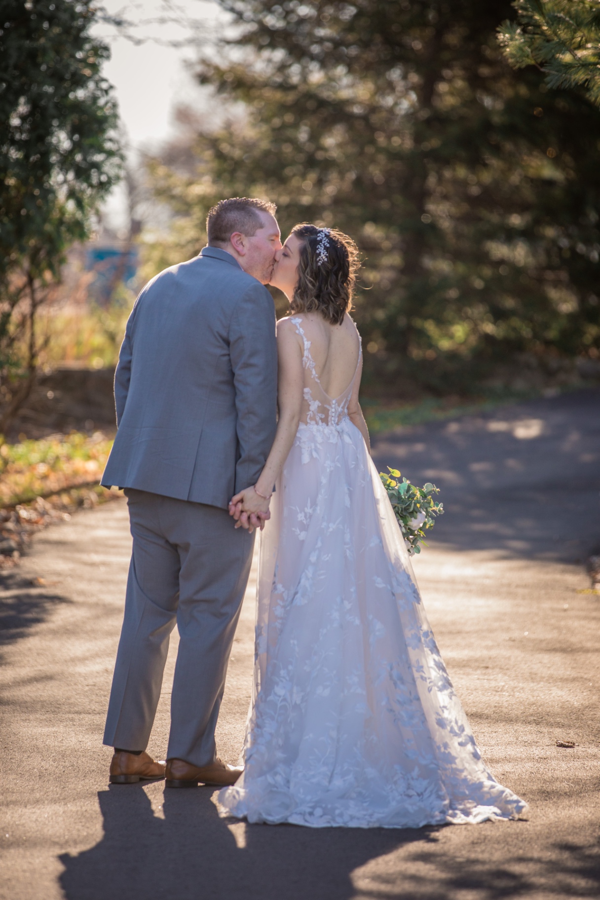Bride and groom share a gentle kiss while walking, sun-dappled and candid