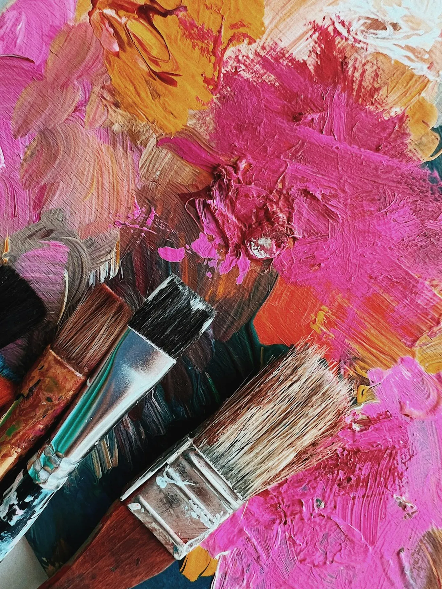 Three well-used paintbrushes resting on a vibrant, textured palette with thick swathes of paint.