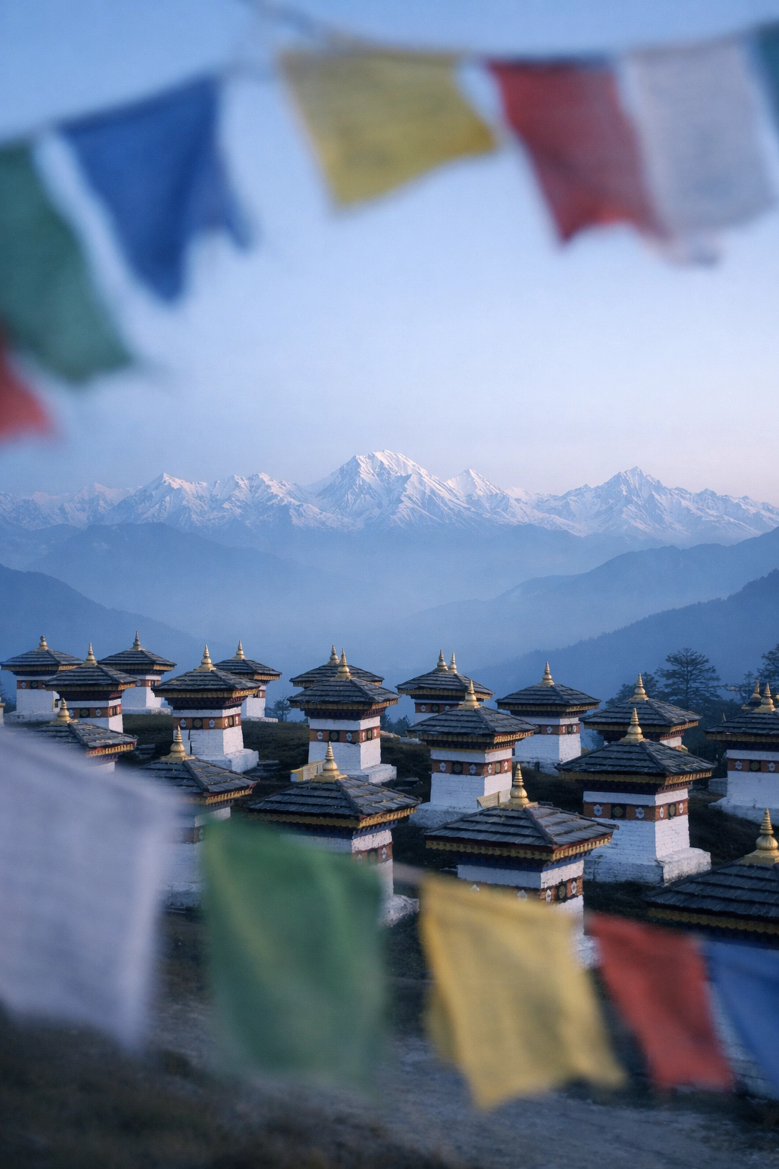 The 108 memorial chortens at Dochu La Pass with prayer flags and snowy Himalayan mountain peaks.