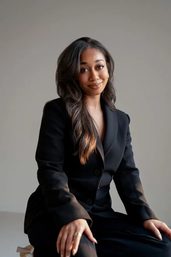 A confident woman in a black suit sitting in a modern studio, showcasing brand authority