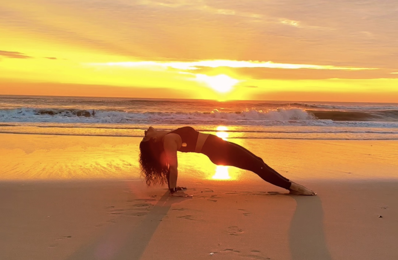 A woman practices yoga on the beach at sunrise