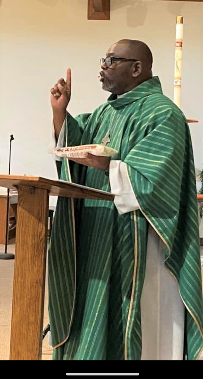 A clergy member in green vestments delivering a sermon from a pulpit