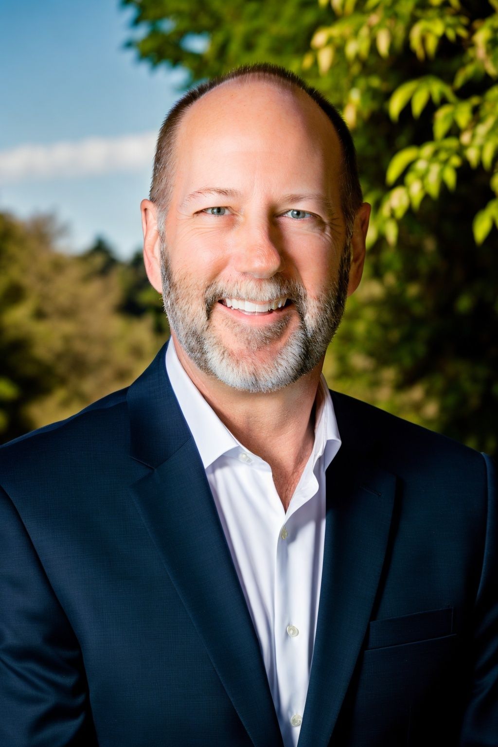 Professional headshot of a smiling man in a navy blue suit, reflecting approachability and professionalism.