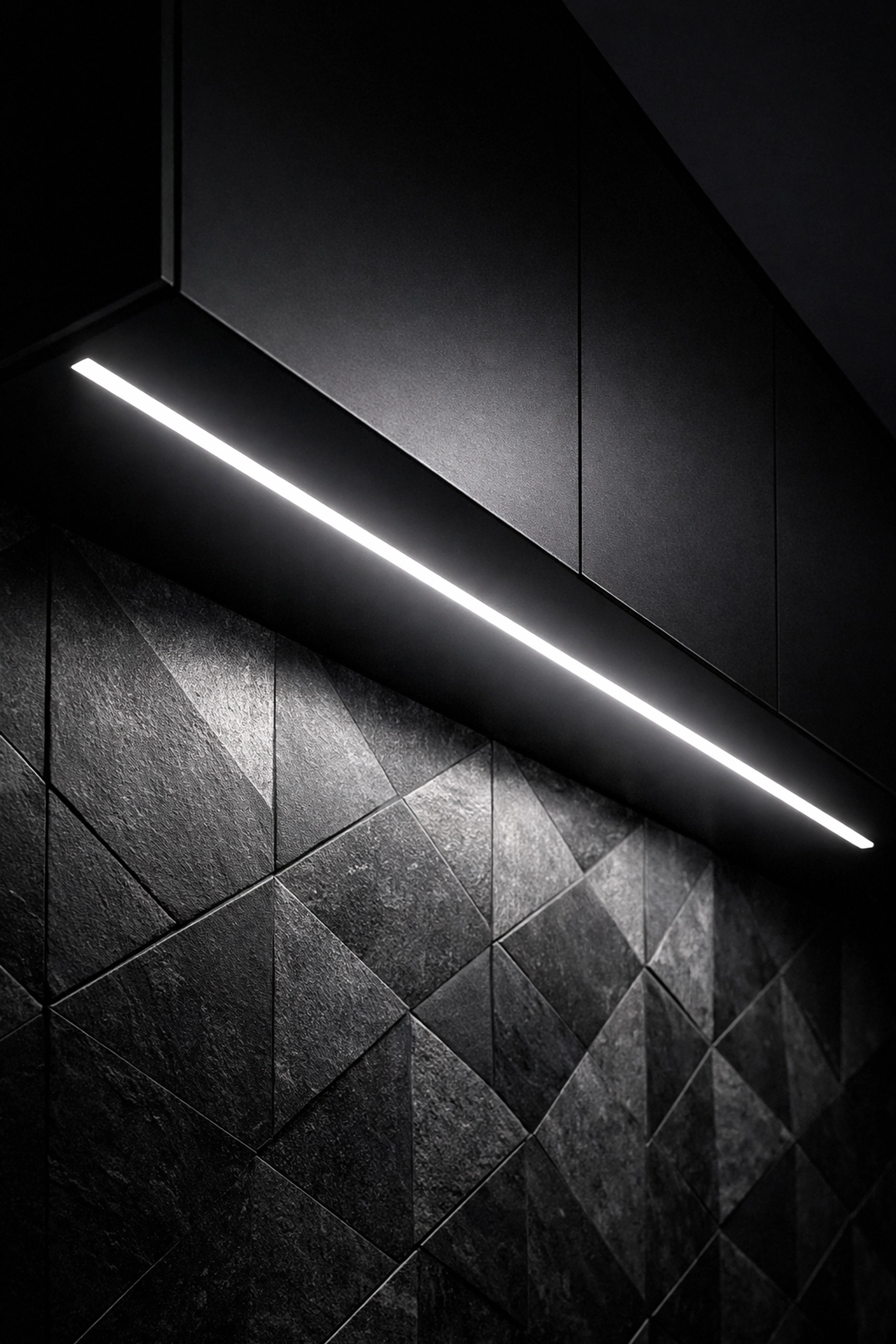 Integrated LED linear light strip under black cabinets providing uniform light on a kitchen backsplash.