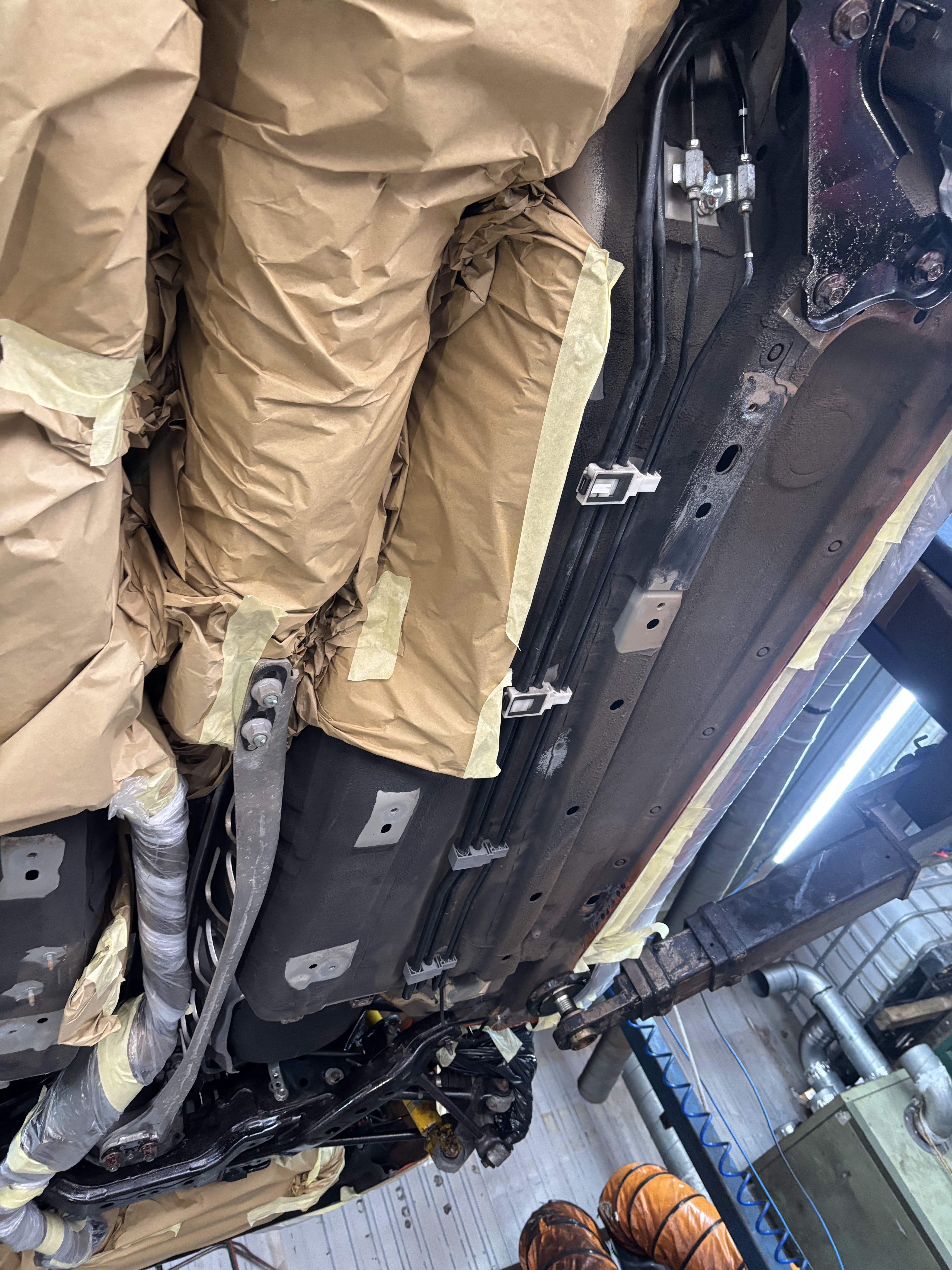 Vehicle underbody prepared for rust proofing, with exhaust and key components masked off using protective paper and tape