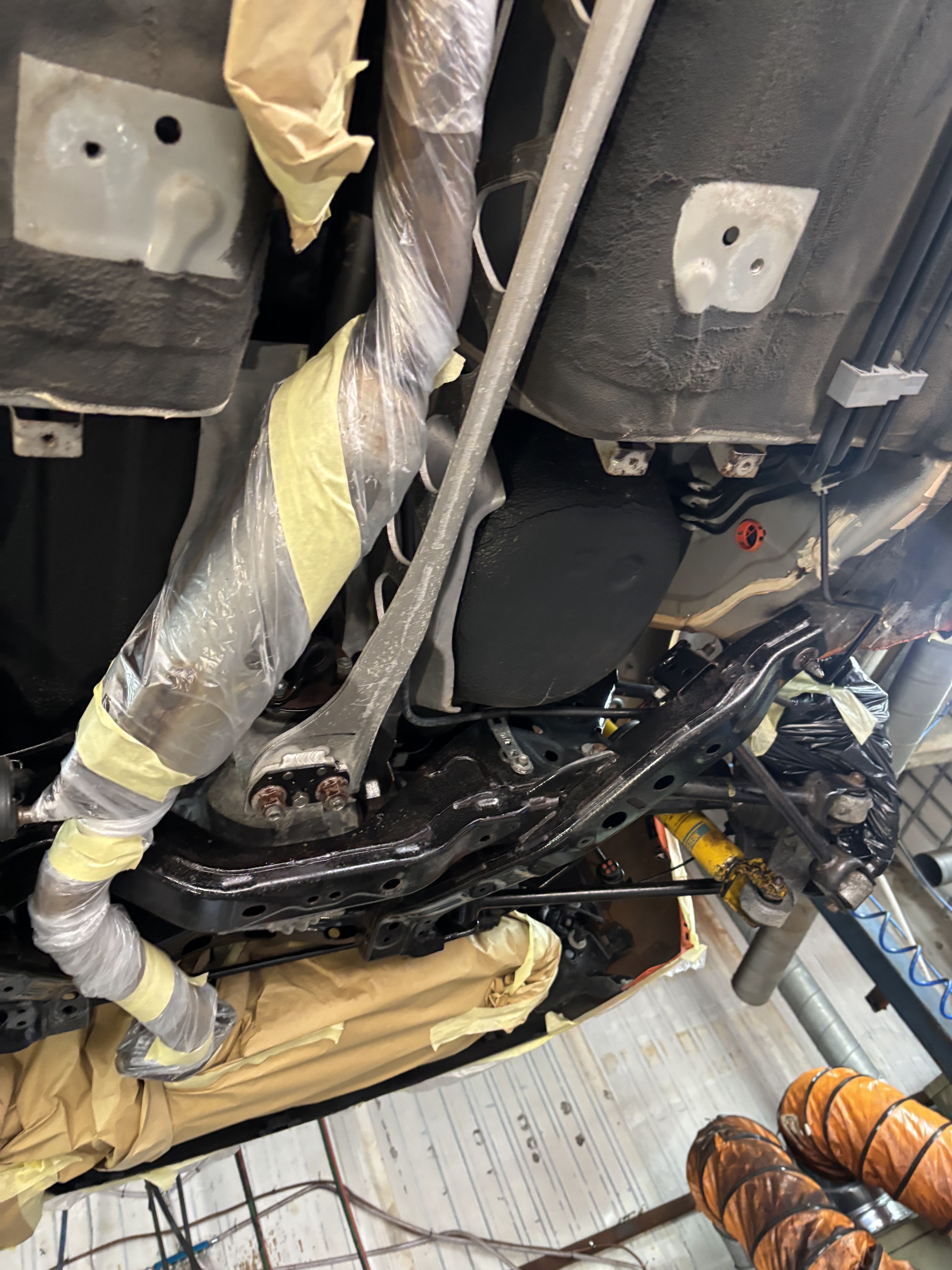 Vehicle underbody on a hoist, with components masked and wrapped in plastic and tape for protection