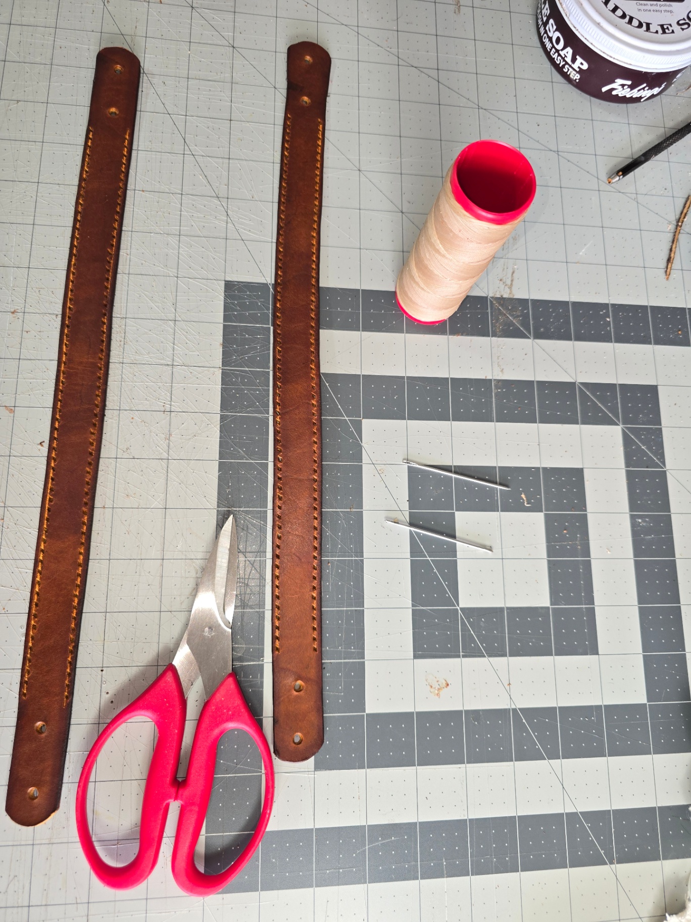 Two hand-stitched brown leather straps with tools