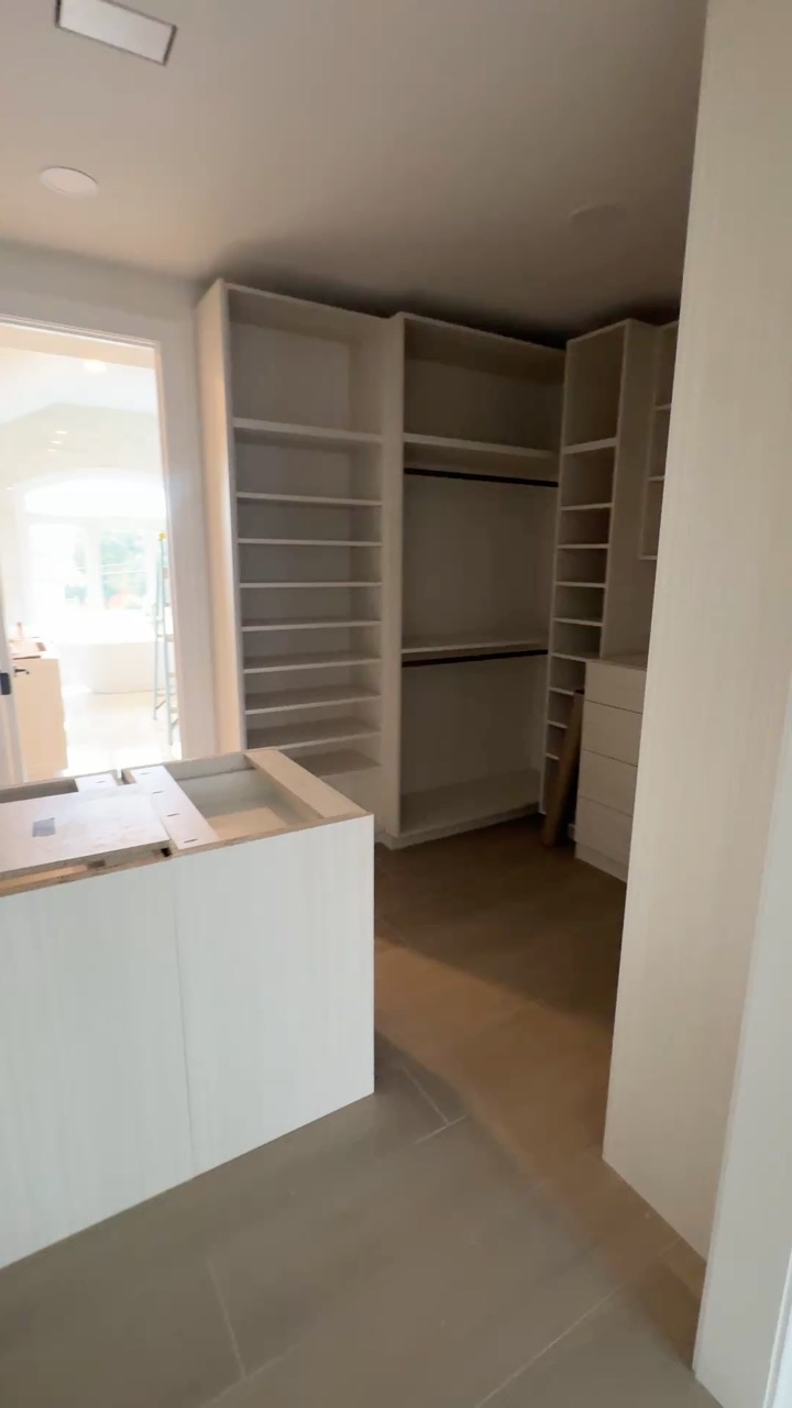 Custom Walk-In Closet Design A walk-in closet featuring built-in adjustable shelving, hanging rods, a drawer unit, and a storage island. Finished in light, modern wood.