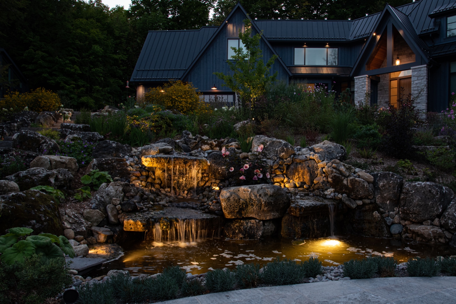Landscape lighting highlights a multi-tiered waterfall and pond feature