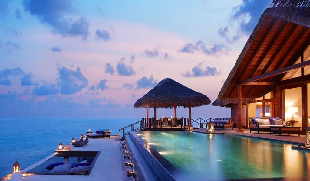 Private luxury overwater villa with infinity pool, sunken lounge area, and direct ocean views at sunset.