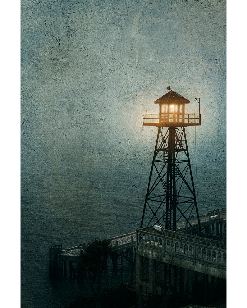 A distant lighthouse beam cutting through night air between dark trees