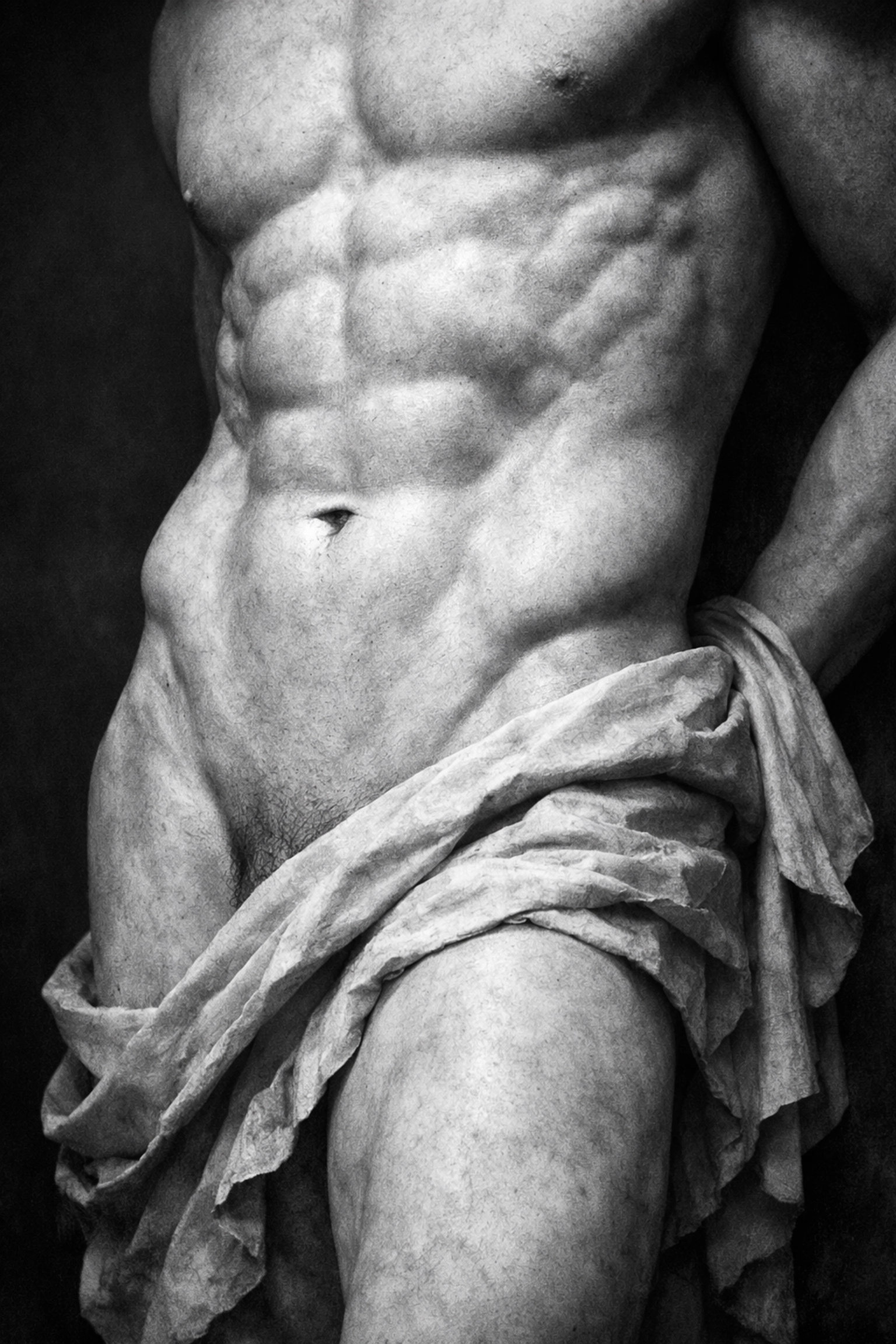 Artistic black and white photo of a man's defined lower abdomen and V-line in classical Greek style.
