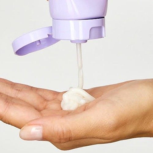 A close-up of an all-natural, Japanese botanical-inspired hair treatment being dispensed from a pastel purple bottle onto a hand
