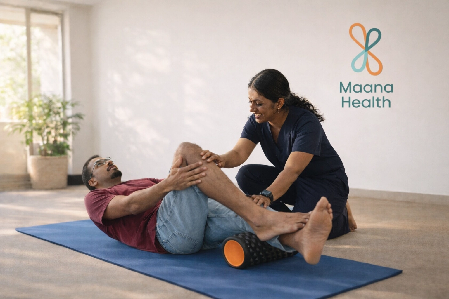 A patient is lying on a mat using a foam roller under their legs for myofascial release while a physical therapist supervises