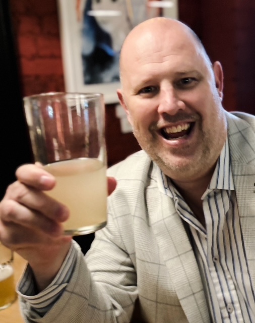 A smiling guest raises a pint of hazy craft beer inside the Lost and Found taproom