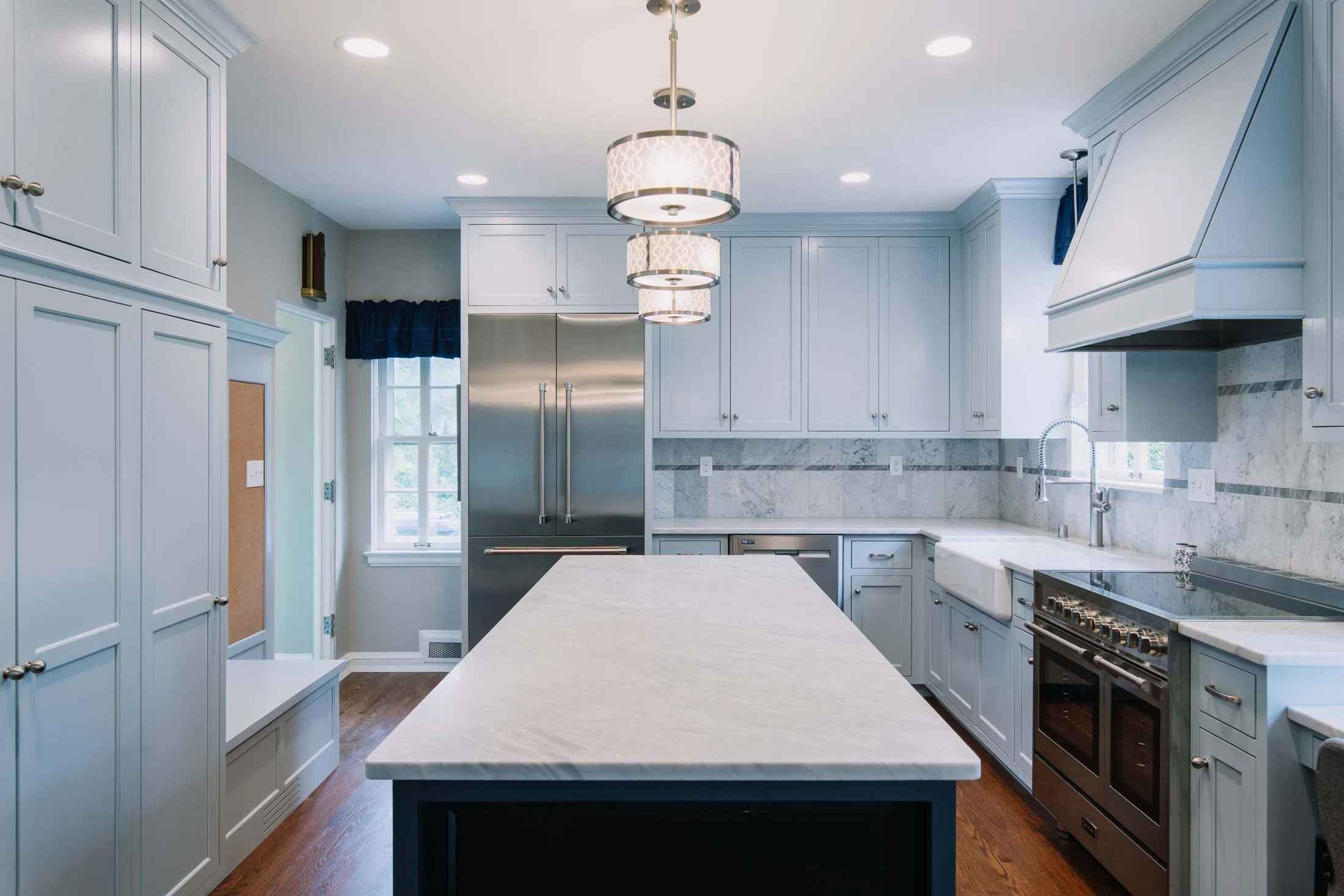 Custom kitchen featuring full-height shaker-style cabinetry in light blue, a large central island with marble-look countertop.