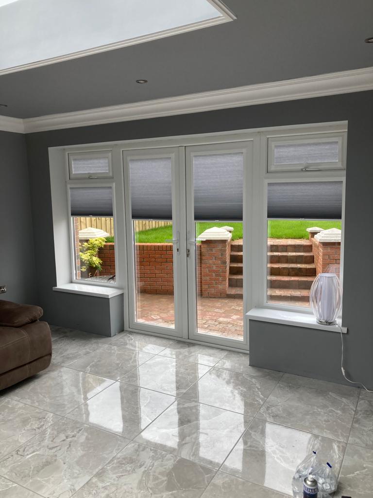 Modern living space featuring custom grey top-down window blinds precision-fitted to French doors, demonstrating tailored in-house manufacturing.