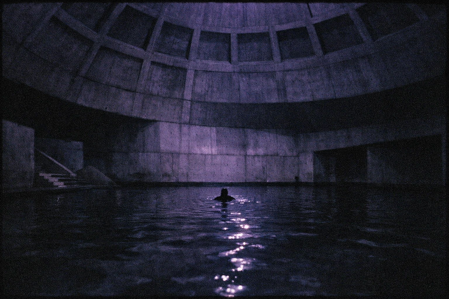 Person floating in the dark Liquidrom Berlin saltwater pool under a massive concrete dome with violet light.
