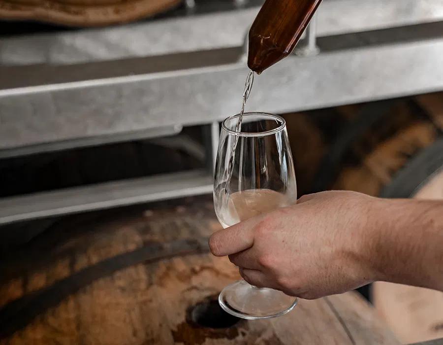 A small-batch spirit is being poured from a barrel sample thief into a tasting glass.