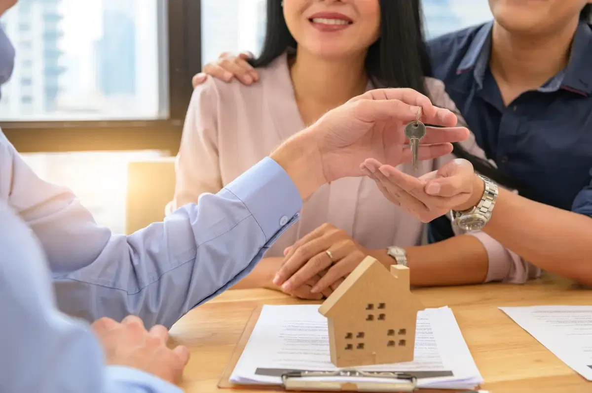 A property manager handing house keys to a smiling couple, representing successful residential leasing.