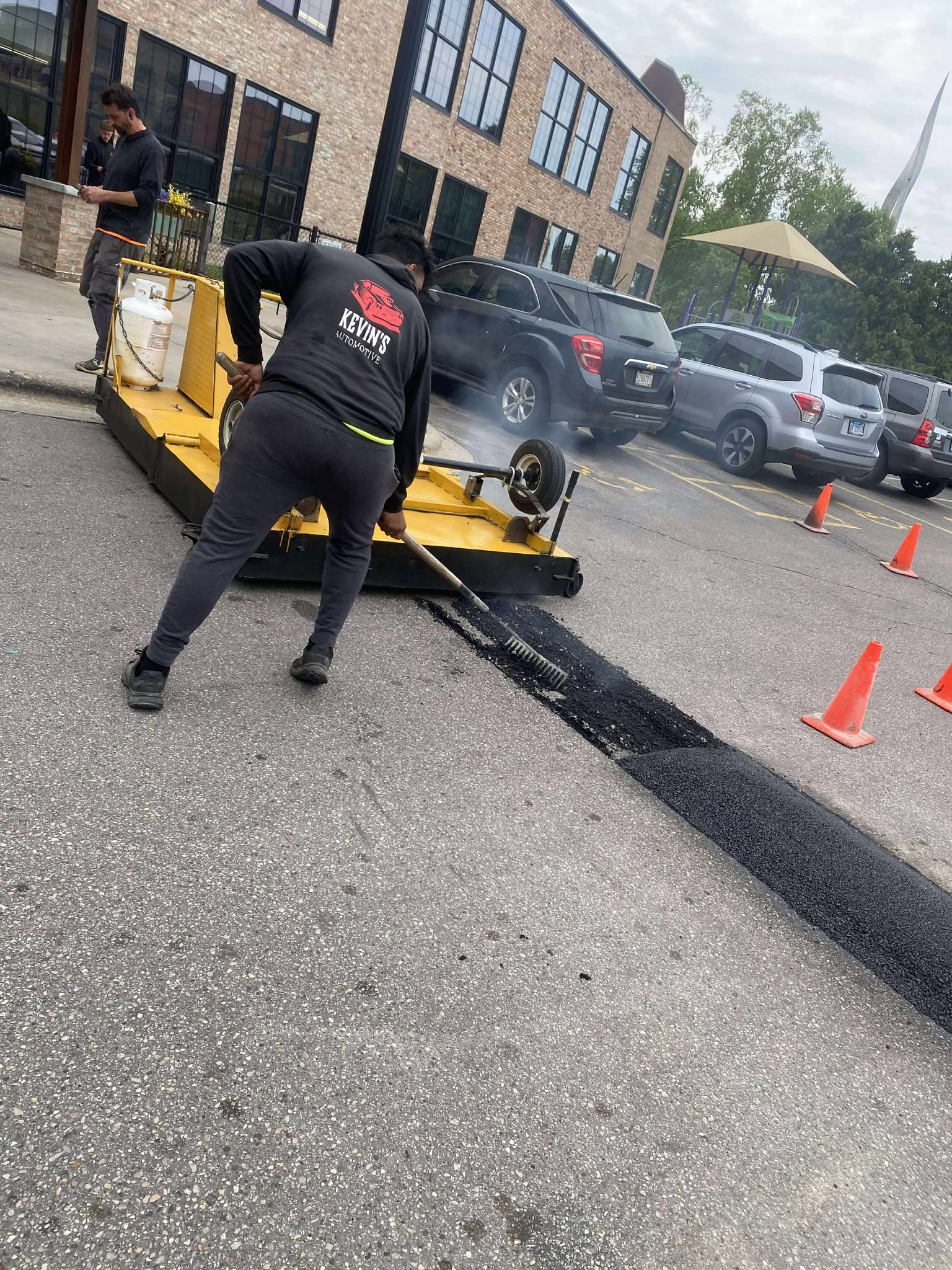 Crew member using specialized equipment to patch and repair a section of asphalt parking lot