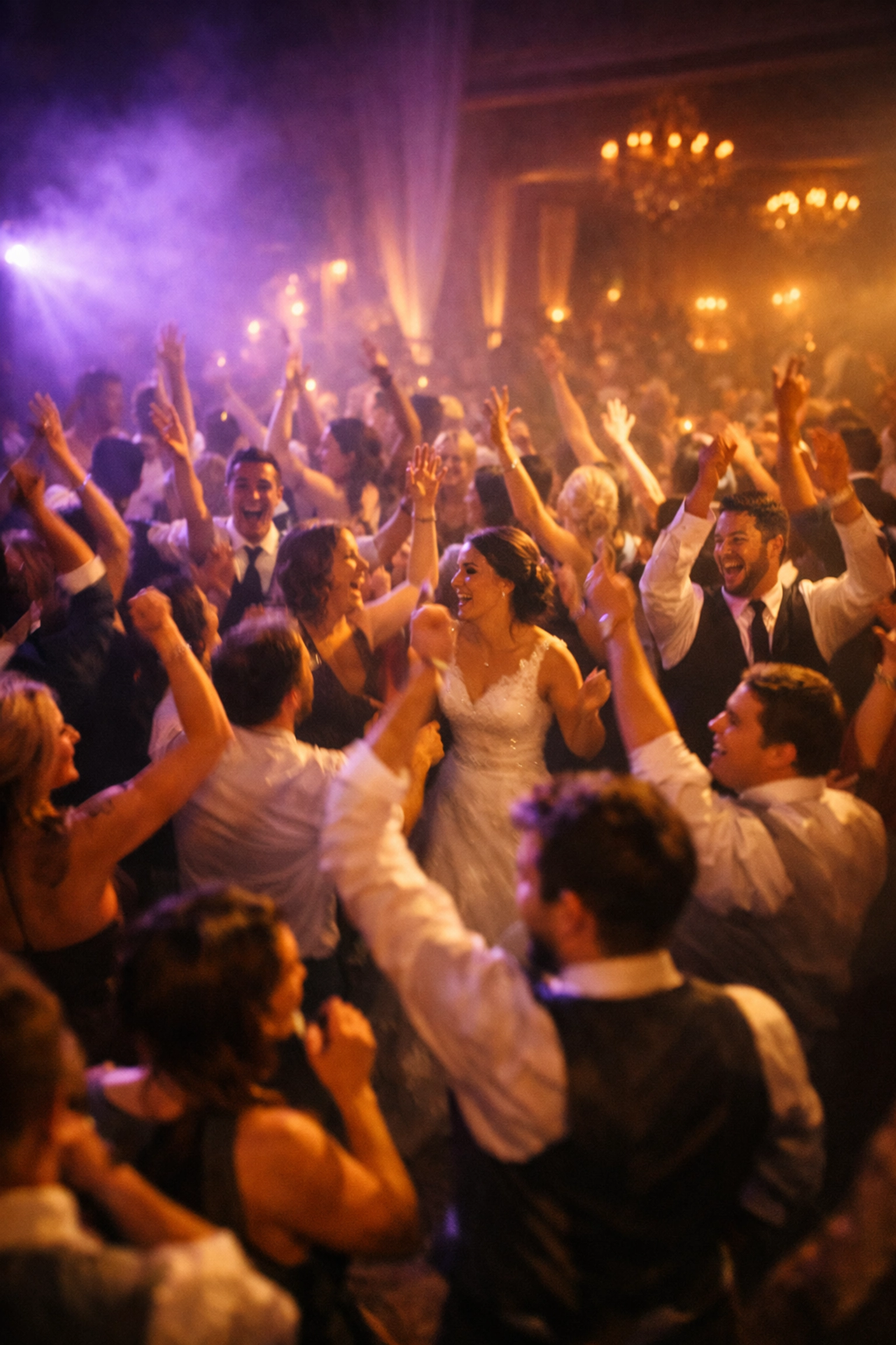 Wedding guests dancing energetically on packed dance floor under dramatic purple and amber uplighting