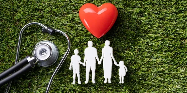 Stethoscope, red heart, and paper-cutout silhouette of a family of four on grass
