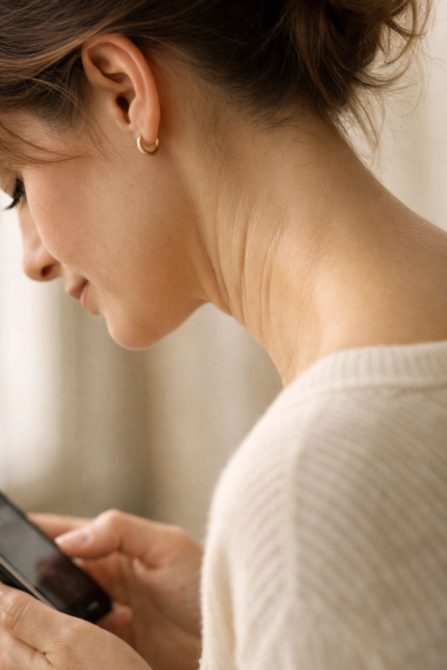 Woman demonstrating tech neck posture looking down at smartphone showing horizontal neck lines and creasing
