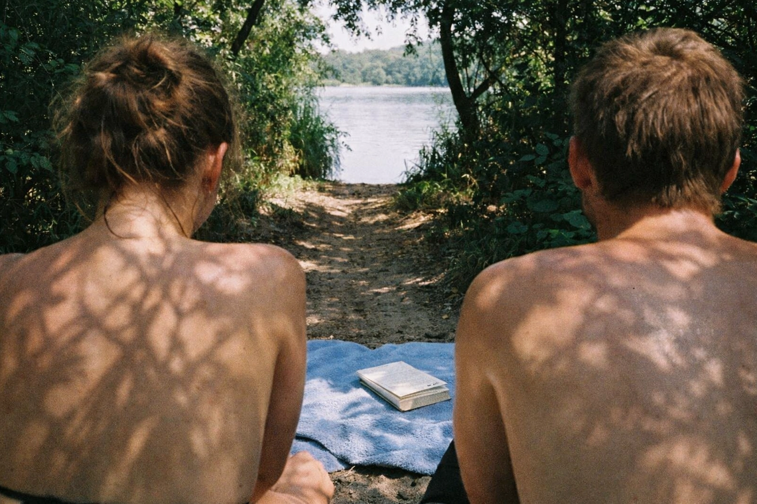 Halensee quiet hideout: dense scrub and trees, narrow sandy path, pale skin with tree shadows, towel and book.