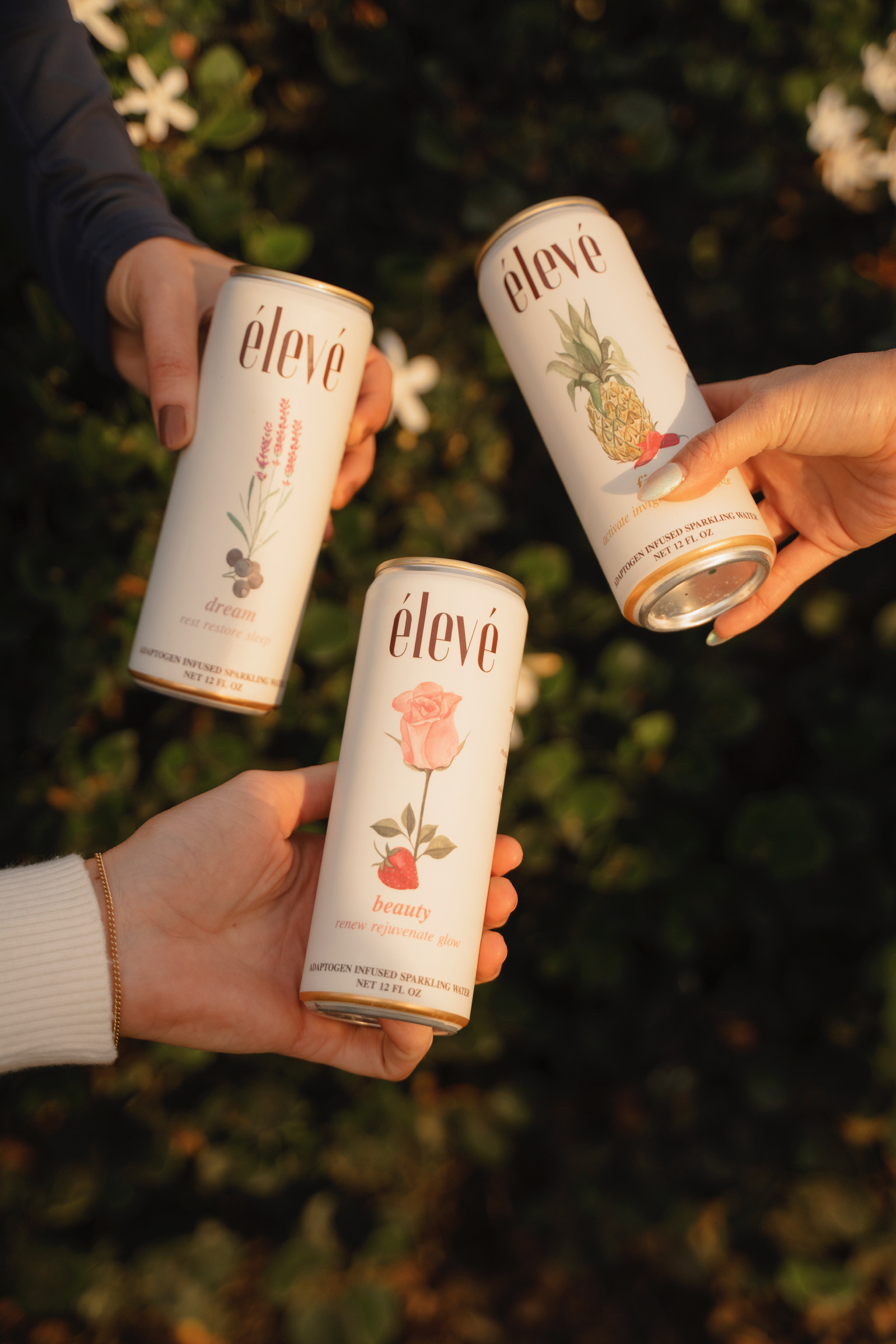 Three hands holding élevé adaptogen-infused sparkling water cans