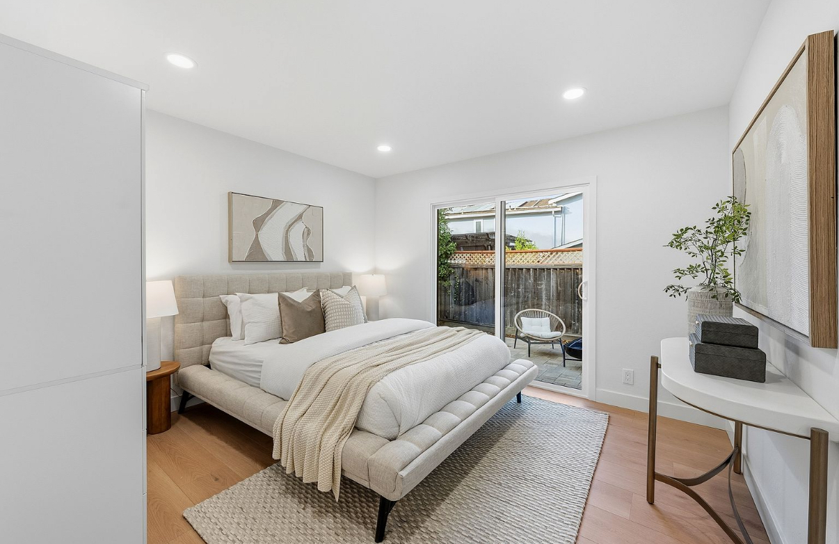 Staged Modern Bedroom A staged modern bedroom featuring neutral tones, stylish decor, an upholstered bed with accent pillows, abundant natural light from sliding glass doors leading to a private patio, hardwood flooring, and a cozy rug. The setup creates a welcoming atmosphere that showcases ideal South Bay living.