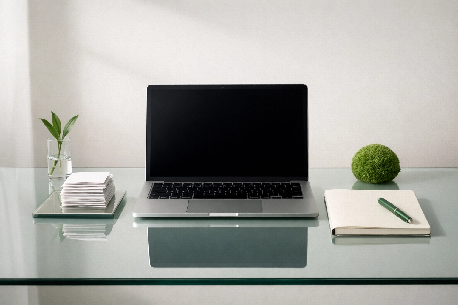 High-end minimalist glass desk with a sleek laptop, blank ledger materials, and subtle green botanical accents representing accrual accounting discipline.