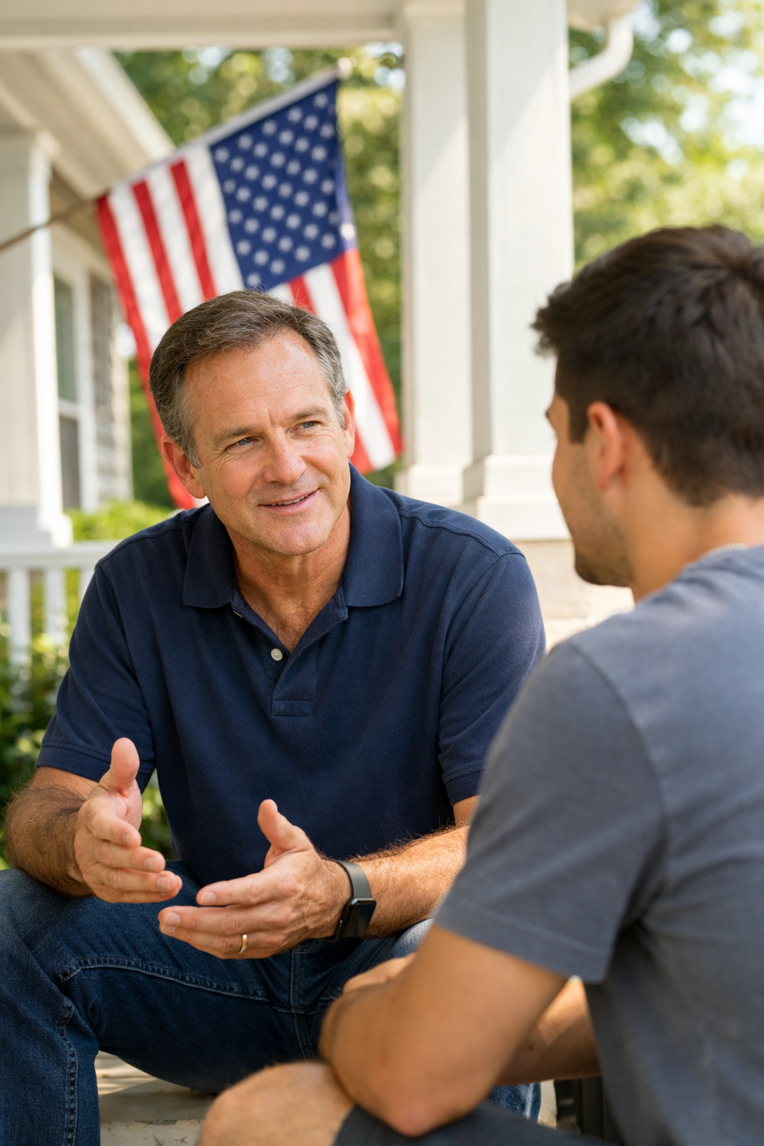 A man providing community leadership and mentorship on a porch featuring a patriotic American flag background.