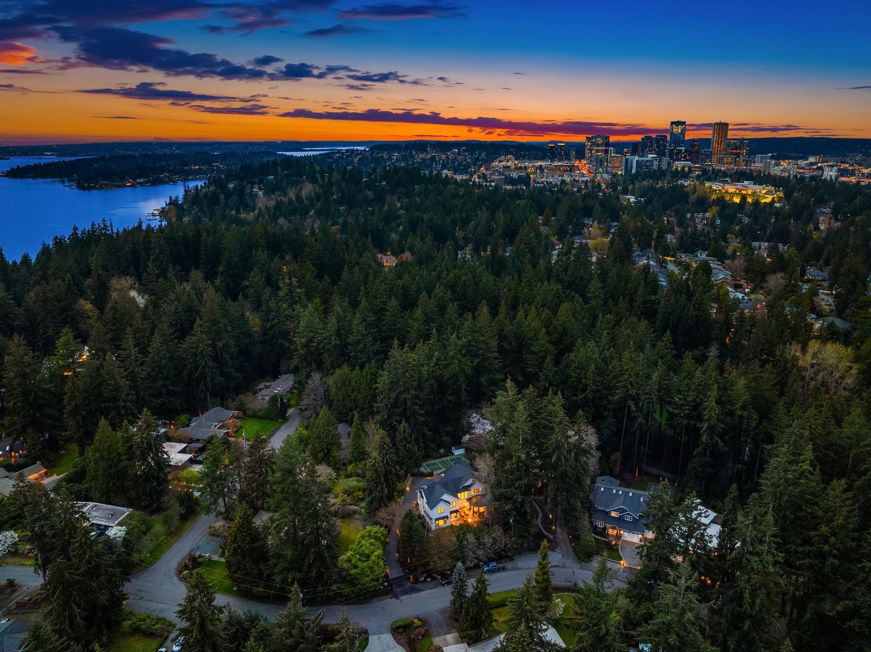 Aerial twilight view showing the wooded neighborhood and city skyline