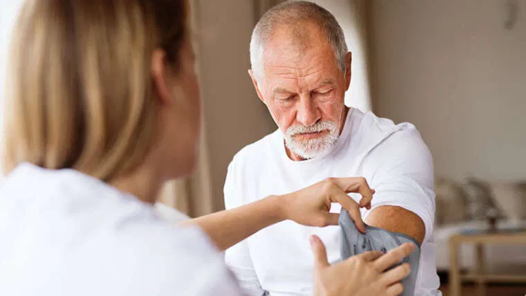 A nurse checks the blood pressure of an elderly man at home, demonstrating Hand in Hand Care’s skilled nursing and personalized health monitoring services