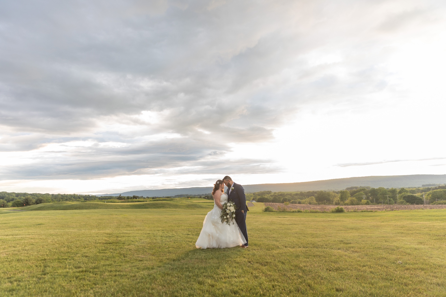 Natalie and Pat embracing in an open field at sunset