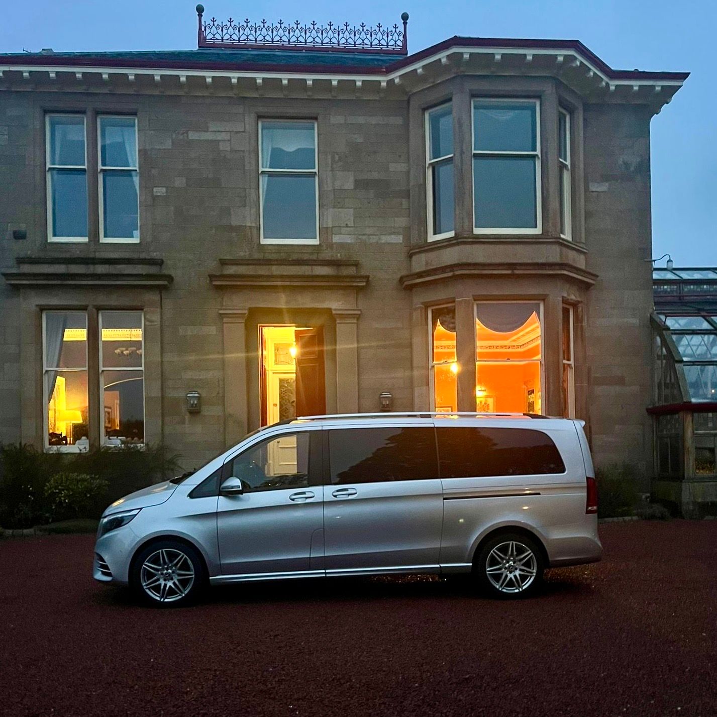 Luxury Mercedes-Benz chauffeur vehicle parked outside an elegant property at dusk