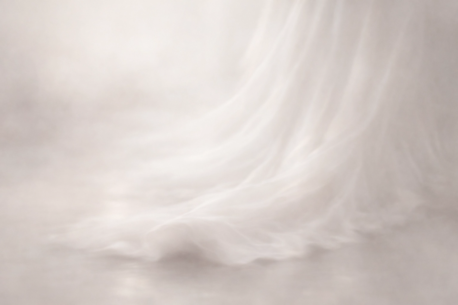 A dreamy, out-of-focus glimpse of a white silk bridal gown trailing elegantly on the floor.