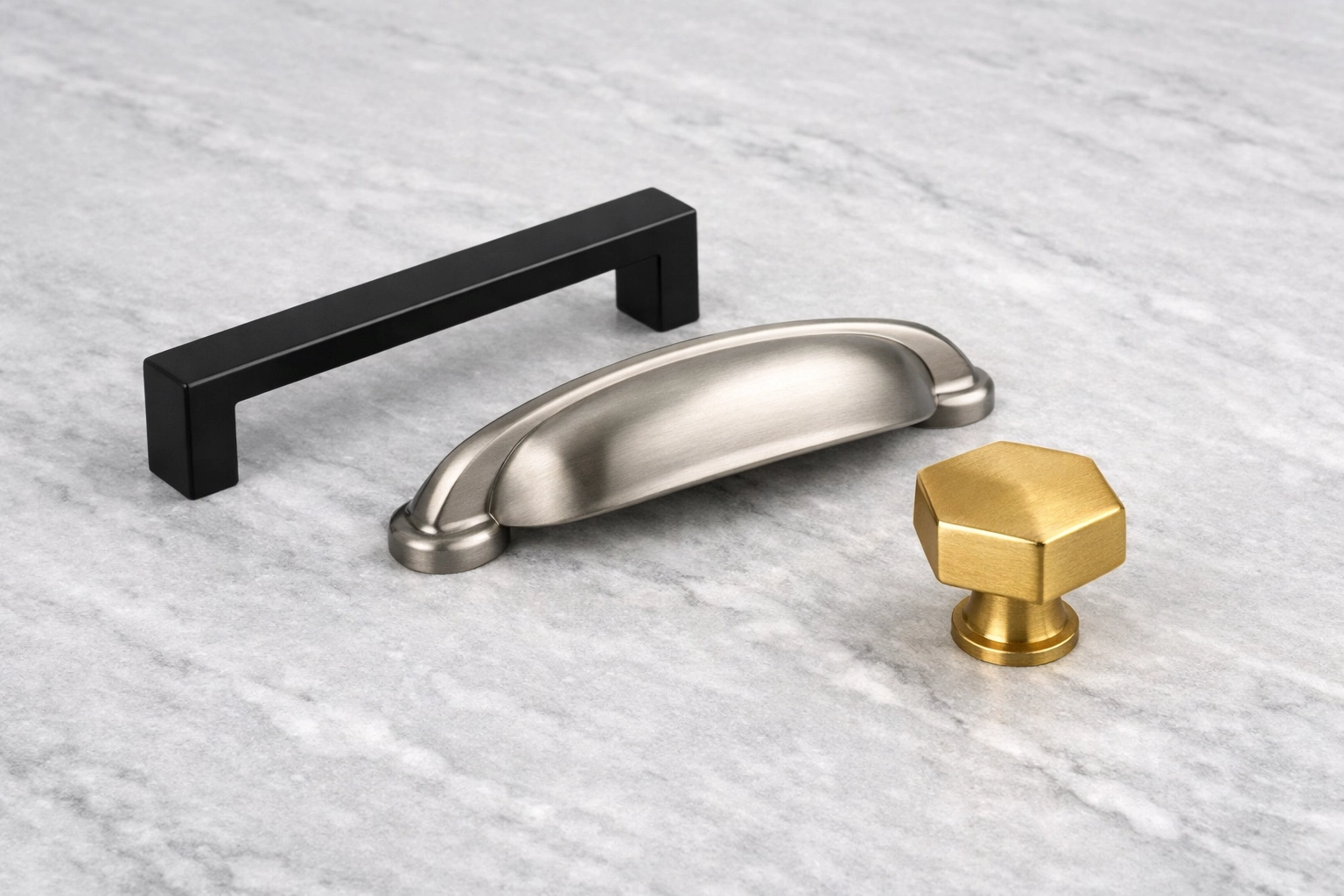 Modern kitchen cabinet hardware finishes including matte black and gold on a marble countertop.